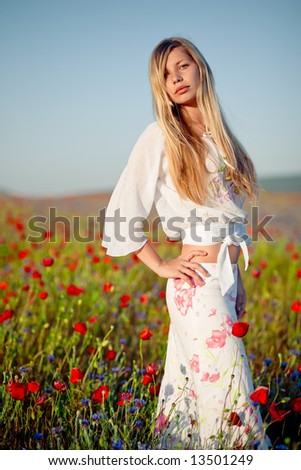 Nice blond woman with long hair staying in field of flowers