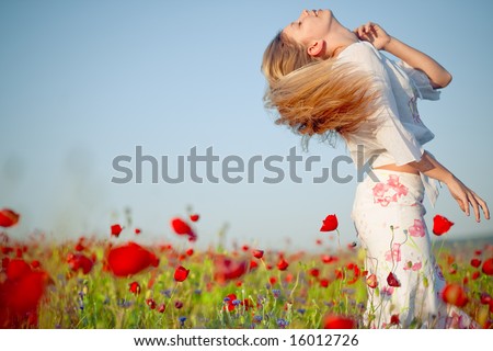 Blond girl with beautiful long hair in field of poppies in summer