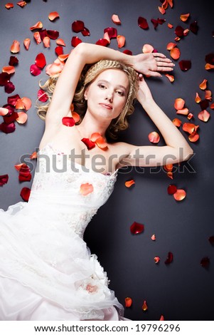 Beautiful sexy bride lying on the floor among red rose petals on gray background