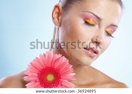 Portrait of beautiful female holding pink daisy with water drops on face