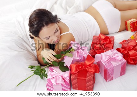 Portrait of beautiful woman with rose and gifts on bed in morning