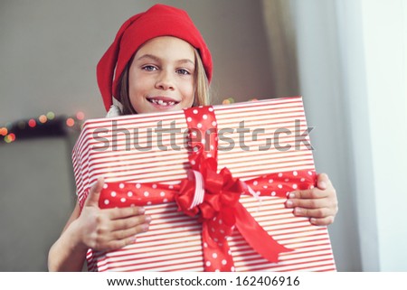Portrait of a pin up kid girl holding big Christmas gift box on blue vintage wooden background