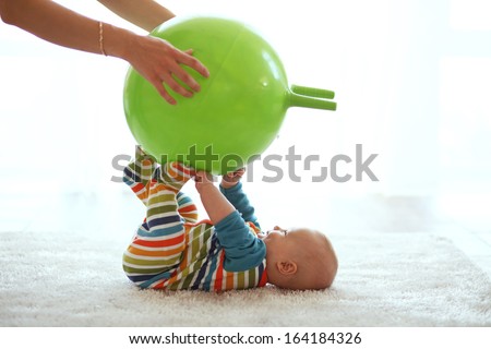 Baby playing with gymnastic ball with mother at home