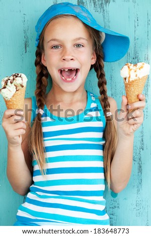 Portrait of 7 years old kid girl eating tasty ice cream on blue background