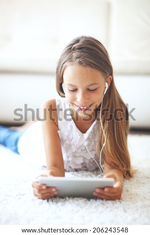 Pre teen girl playing on tablet pc laying down on a white carpet at home