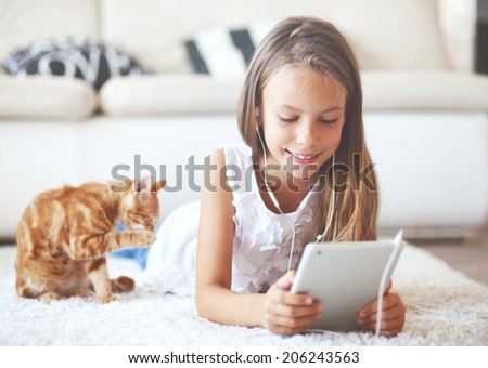 Pre teen girl playing on tablet pc laying down on a white carpet at home Pre teen girl playing on tablet pc laying down on a white carpet at home