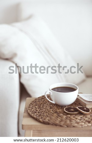 Still life interior details, cup of coffee and a book near white cozy chair