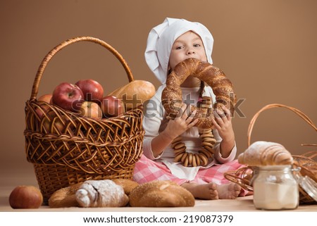 5 years old girl baker eating bakery products, studio shot