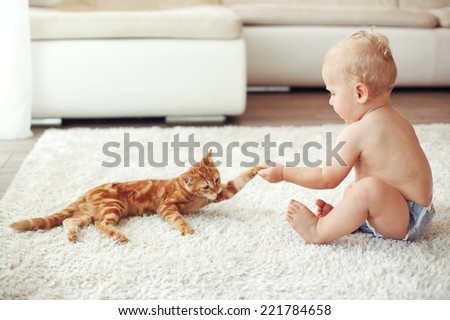 Toddler playing with red cat on a white carpet at home