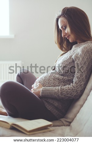 Home cozy portrait of pregnant woman resting at home and reading book on sofa