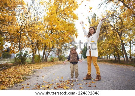 Young mother with her little daughter walking in fall park on yellow fallen leaves one autumn day