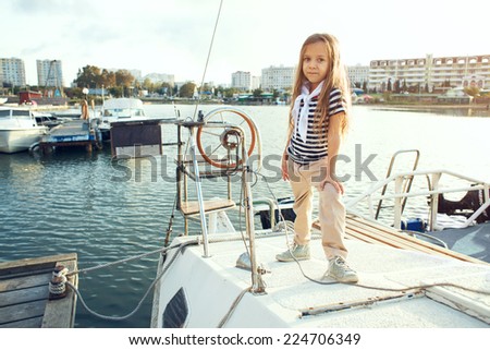 Fashion child wearing navy clothes in marine style posing on white yacht in sea port