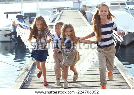 Group of 4 fashion kids wearing striped navy clothes in marine style running in the sea port