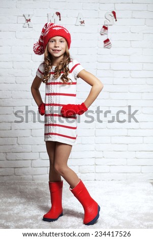 Little fashion girl in fashion Christmas clothes posing over white brick background, full length