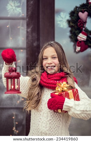 Child girl welcome guests and holding presents, snow weather, house door is decorated before Christmas
