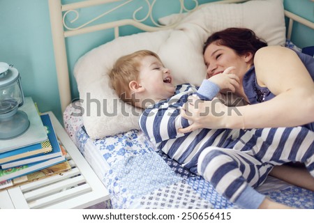 Young mother playing with her 2 years old little son at the bedroom