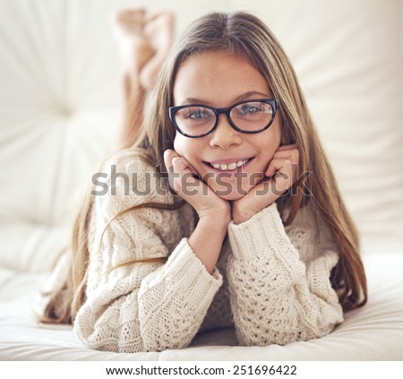 Home portrait of 8 years old school girl wearing glasses resting on the sofa, looking at camera