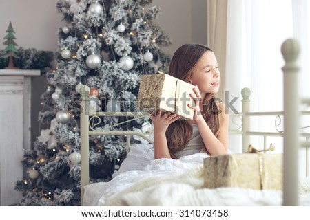 Preteen child girl wake up in her bed near decorated Christmas tree in beautiful hotel room in the holiday morning, enjoing with presents