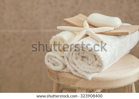 Hotel bathroom decor closeup. White towels, soap, loofah and starfish on wooden stool over stone tile. Natural colors, still life.