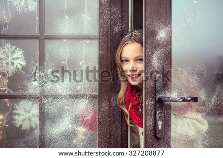 Child girl opens door and welcome guests, snow weather, house is decorated for Christmas