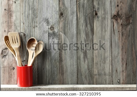 Kitchen cooking utensils in ceramic storage pot on a shelf on a rustic wooden wall, space for text