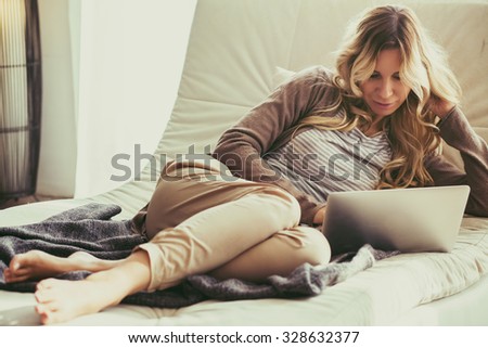 Happy young woman is relaxing on comfortable couch and using laptop at home. Photo toned.