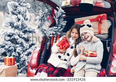 Holiday preparations. Pre teen children enjoy many Christmas presents in car trunk. Cold winter, snow weather.