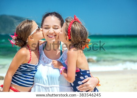 Mom with her two children having fun at the tropical beach, daughters kissing mother