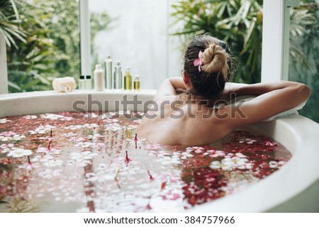 Woman relaxing in round outdoor bath with tropical flowers, organic skin care, luxury spa hotel, lifestyle photo