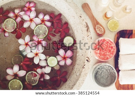 Foot bath in bowl with lime and tropical flowers, spa pedicure treatment, top view