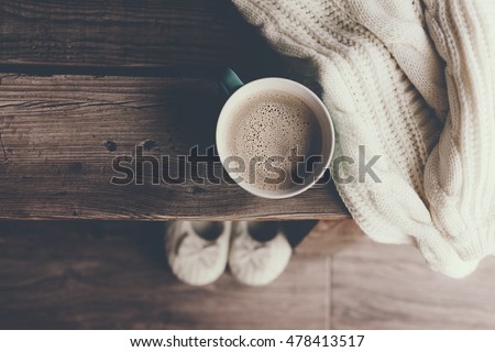 Cup of hot coffee on rustic wooden bench, closeup photo of warm sweater with mug and slippers, winter morning concept, top view