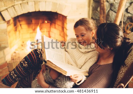 Mom with child reading book and relaxing by the fire place some cold evening, winter weekends, cozy scene
