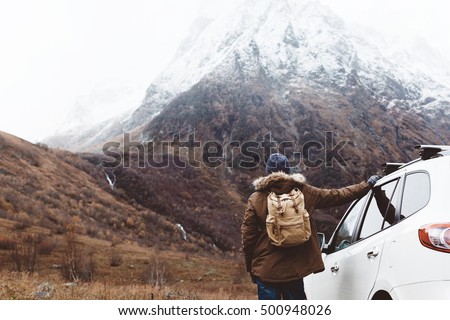 Man driving car on to the mountains. Traveler with backpack. Hiking in cold weather.