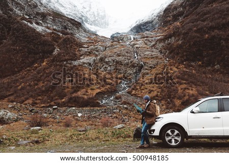 Man driving car on to the mountains. Traveler with backpack looking map. Hiking in cold weather.