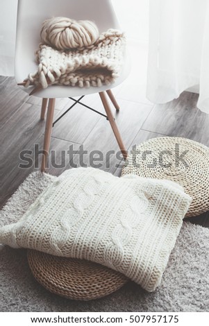 Knitted blanket on wicker ottoman, modern plastic chair in living room. Details of white scandinavian interior.