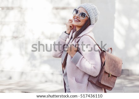 Young stylish woman wearing pink warm coat, pants and handbag walking in the city street in cold season. Winter fashion, elegant look, outfit in pastel colors. Plus size model.