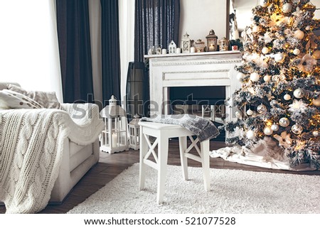 Beautiful holiday decorated room with Christmas tree, fireplace and armchair with blanket. Cozy winter scene. White interior with lights.