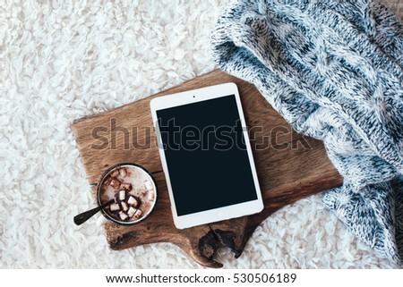 Winter homely scene, scandinavian style. Warm knit sweater, tablet pc with blank screen and cup of sweet cocoa with marshmallows on wooden tray in bed. Lazy cold weekend.