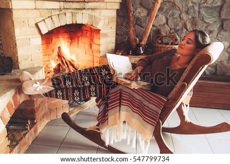 Woman reading book and relaxing by the fire place some cold evening, winter weekends, cozy scene