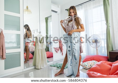 10 years old pre teen girl choosing outfit in her closet. Messy in the bedroom, clothning on the floor. Teenager is dressing up and singing in the morning.