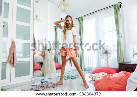 10 years old pre teen girl choosing outfit in her closet. Messy in the bedroom, clothing on the floor. Teenager is dressing up and dancing in the morning.