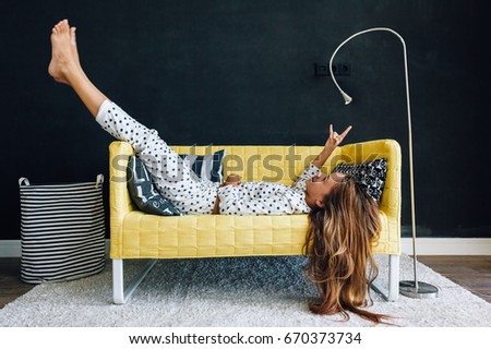 Home portrait of pre teen child girl wearing pajama relaxing and chilling on the yellow couch against black wall in modern living room interior