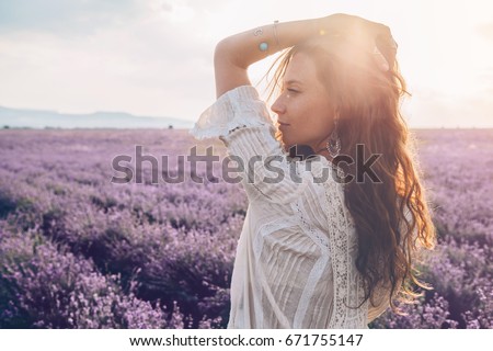 Beautiful model walking in spring or summer lavender field in sunrise backlit. Boho style clothing and jewelry.