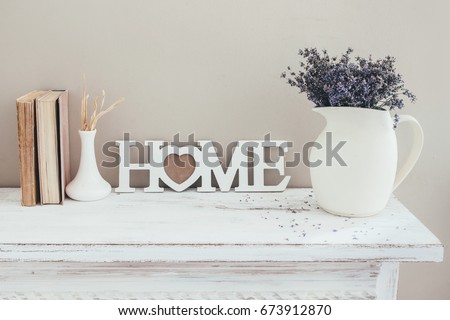 Shabby chic interior decor for farmhouse. Lavender in pitcher, books and wooden letters on a vintage shelf over pastel wall. Provence home decoration.