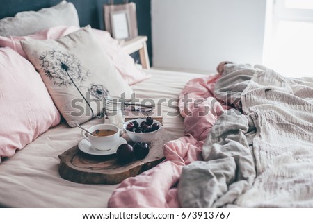 Black loft bedroom and pastel bedding set. Unmade bed with breakfast and reading on tray. Interior decor over blackboard wall. Cozy modern living space.