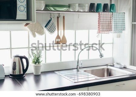 Home kitchen interior. Cooking utensils on a railing system and shelf with dishes above a window.