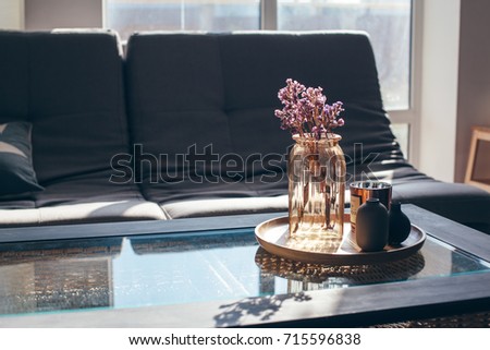 Home interior decor in gray and brown colors: glass jar with dried flowers, vase and candle on the wooden tray on the coffee table over sofa. Living room decoration.