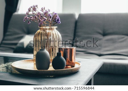 Home interior decor in gray and brown colors: glass jar with dried flowers, vase and candle on the wooden tray on the coffee table over sofa. Living room decoration.