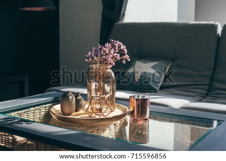 Home interior decor in gray and brown colors: glass jar with dried flowers, vase and candle on the wooden tray on the coffee table over sofa with cushions. Living room decoration.