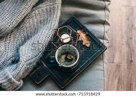 Still life details of living room. A cup of coffee on the rustic wooden tray, candle and warm woolen sweater on the sofa, top view point. Autumn weekend concept. Fall home decoration.